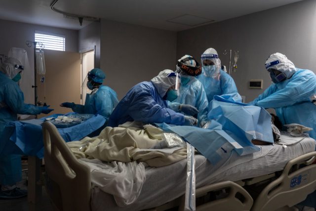 Doctors in protective gear taking care of a patient in a hospital bed