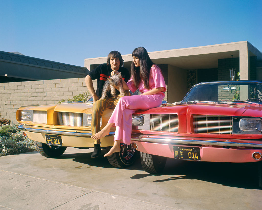 Sonny and Cher sit on a car with their dog