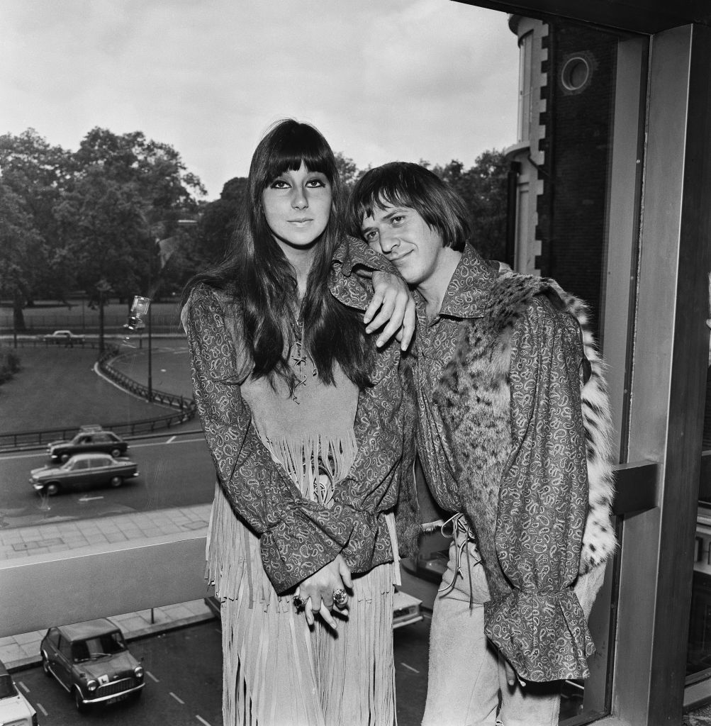 Sonny and Cher pose in front of a window