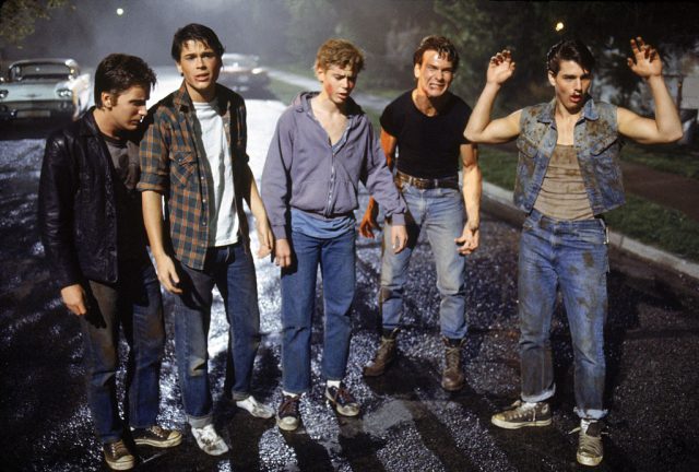 The cast of The Outsiders standing on a street at night
