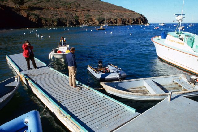 The Prince Valiant floating by the dock, with three individuals looking at it