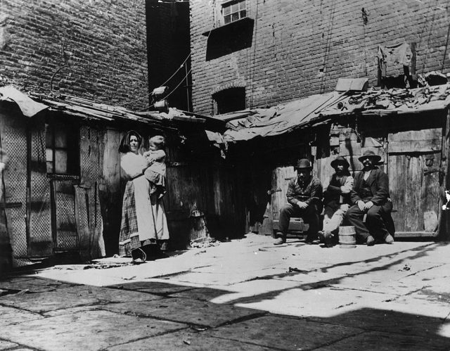 A family standing in front of tenement slums