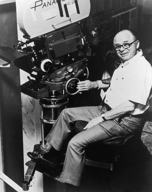 Director Billy Wilder smiles while sitting in front of a camera on the set of one of his films. (Photo Credit: Getty Images)