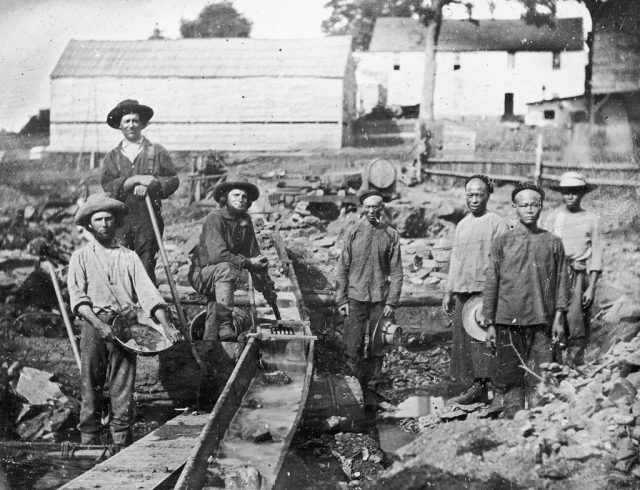Caucasian and Chinese gold miners standing around equipment