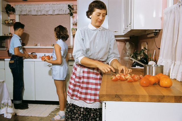 Mother cutting tomatoes while her children stand behind her