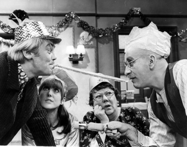 Actor Anthony Booth (left) sharing in some Christmas cheer with Warren Mitchell (right), in a scene from the TV show ‘Till Death Us Do Part’, closely watched by Una Stubbs (second from left) and Dandy Nichols. (Photo Credit: Leonard Burt/Getty Images)