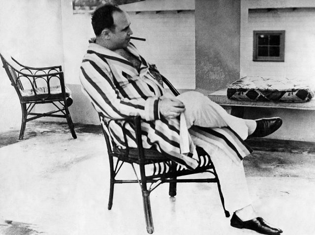 Al Capone sitting in a chair with a cigar in his mouth