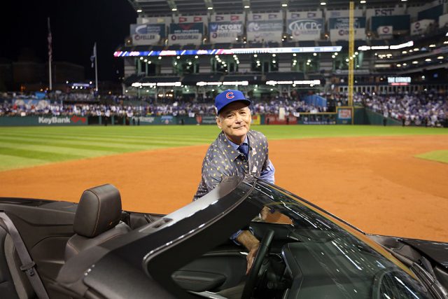 Bill Murray standing beside a convertible on a baseball diamond