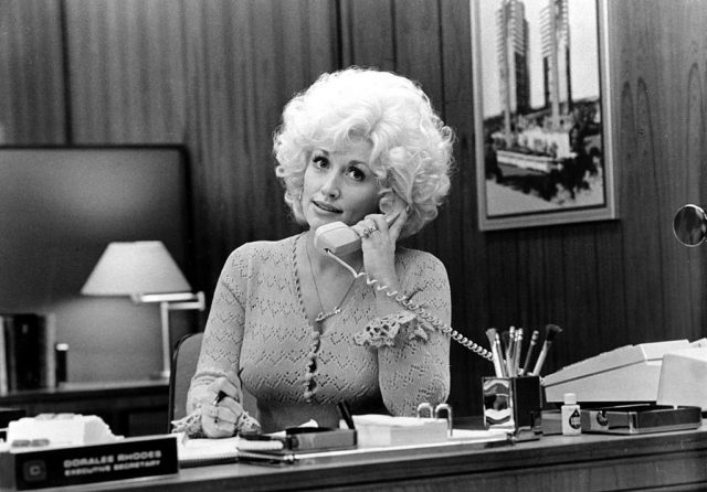 Dolly Parton sitting behind a desk while holding a telephone to her ear