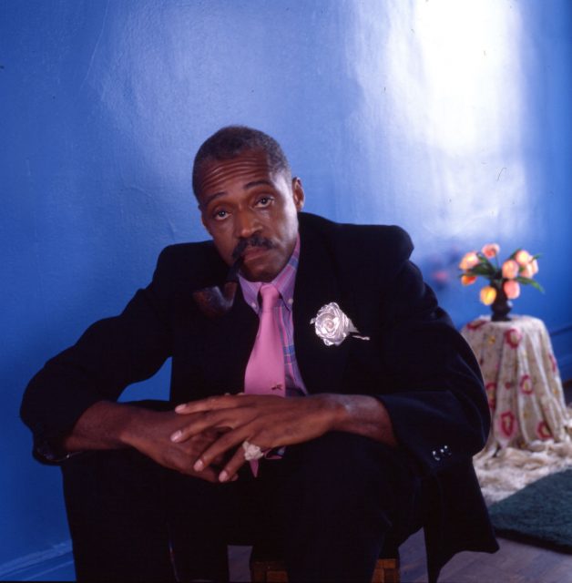 Portrait of American film director, actor, musician, and author Melvin Van Peebles, dressed in black and pink, as he sits in a blue room, New York. (Photo Credit: Anthony Barboza/Getty Images)