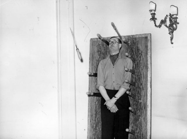 Man standing in front of a wooden board with knives sticking out of it