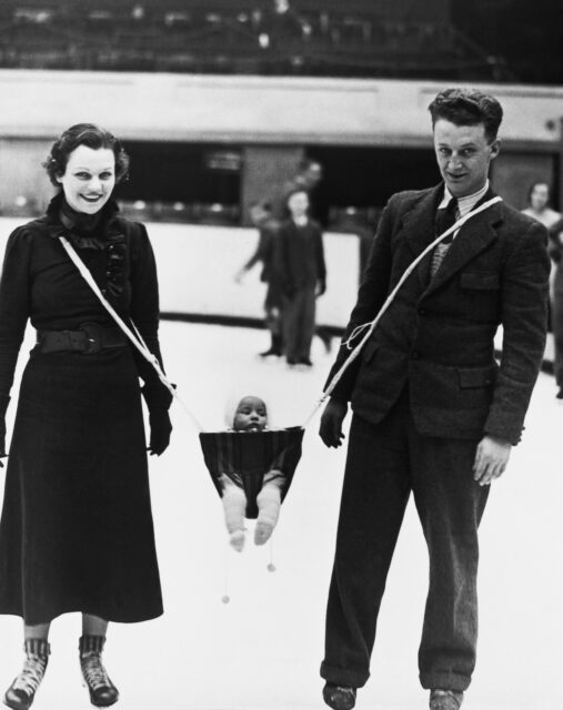 Parents ice skating with their child swinging between them.