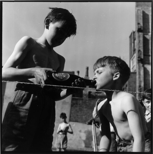 One boy pours beer into the mouth of another boy.