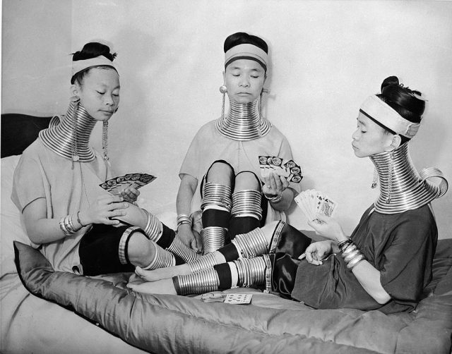 Three Burmese women playing cards atop a bed