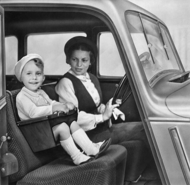 A woman and child in a car, the child in a car seat.