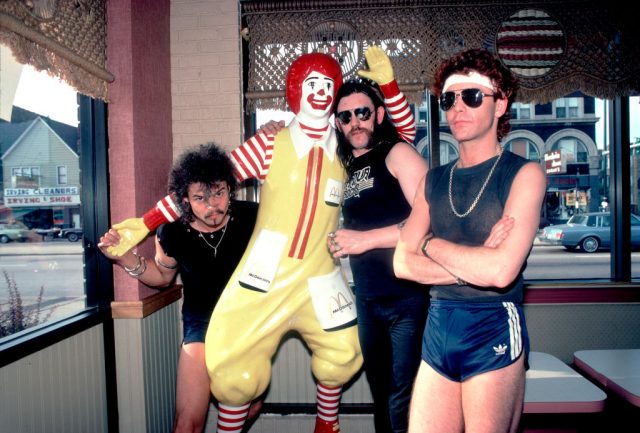 Members of Motörhead standing with a statue of Ronald McDonald