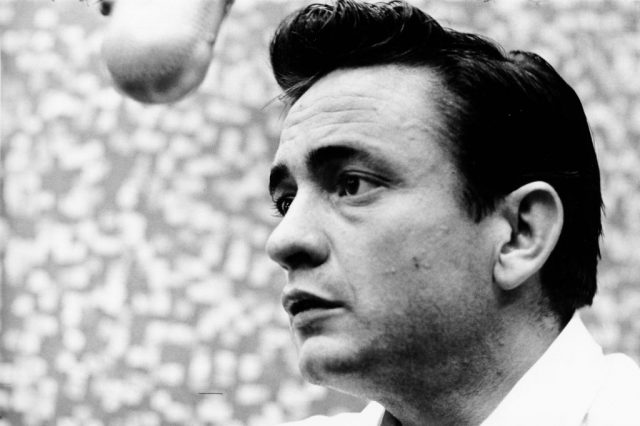 Johnny Cash standing in front of a recording studio microphone