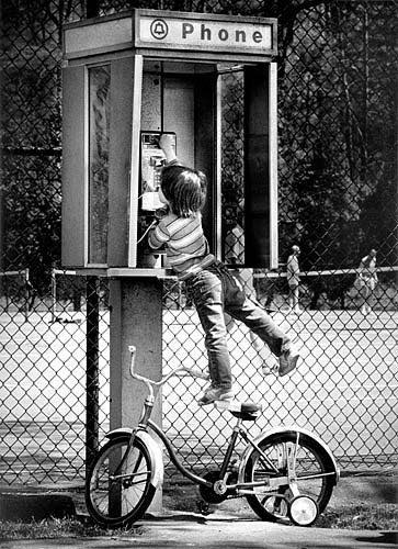 A child standing on his bike trying to reach a payphone 