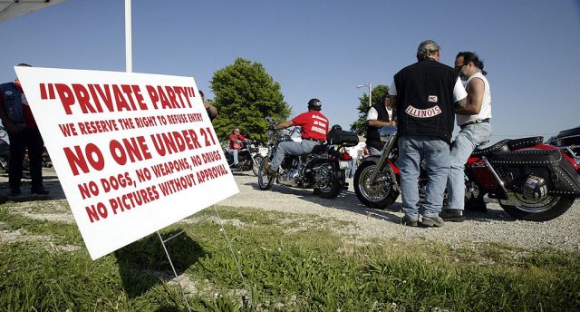 Oz (Back to Camera), a prospect with the Illinois Nomads charter of the Hells Angels, collects a $10 admission from a Harley-Davidson rider at a Hells Angels party June 28, 2003 in Millstadt, Illinois. A prospect is someone going through a trial period hoping to become a full member of the Hells Angels. During the trial period, a prospect is not allowed to wear the Hells Angels name or logo on the back of his vest. (Photo Credit: Scott Olson/Getty Images)