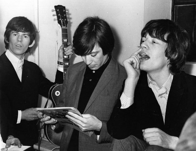 January 1965: Three members of pop group the Rolling Stones backstage, from left to right; guitarist Keith Richards, drummer Charlie Watts and singer Mick Jagger. (Photo Credit: Keystone Features/Getty Images)