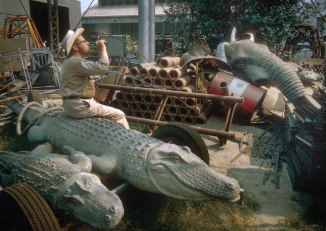 Man sitting on an animatronic alligator while drinking a beverage