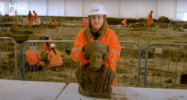 Woman standing behind the bust of an ancient Roman statue