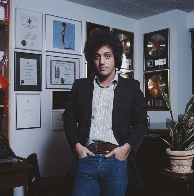 Billy Joel standing in a room with records on the wall