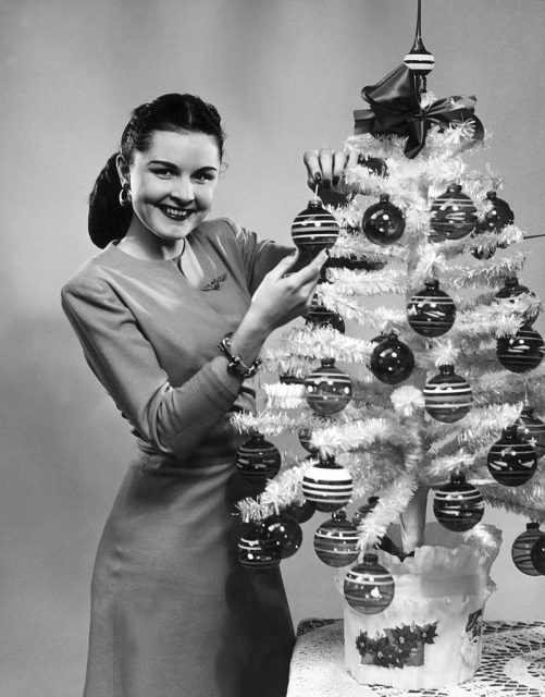 Promotional studio portrait of a woman smiling as she decorates a small plastic Christmas tree with ornaments. (Photo Credit Lambert/Getty Images)