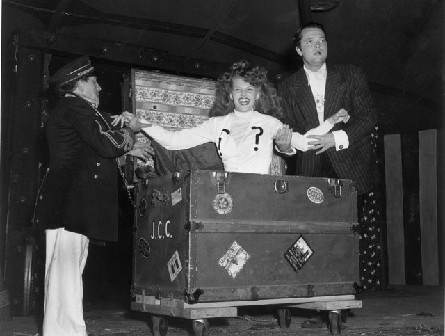 American actor and director Orson Welles and an assistant help American actor Rita Hayworth out of a large trunk