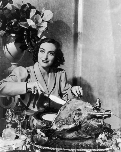 Joan Crawford carving a cooked turkey at the dinner table