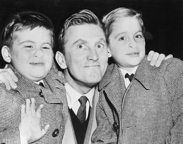 Joel Douglas, left, 6, and Michael Kirk, 9, right, make funny faces for the cameraman with noses pressed against the glass of the U.S. Customs office at Idlewild Airport. The boys, and their dad, Kirk Douglas, center, arrived today from Europe. Douglas is here for TV and Radio appearances in connection with the world premiere, Dec. 24, of his new starring film “Act of Love” (Photo Credit: Bettmann / Contributor)