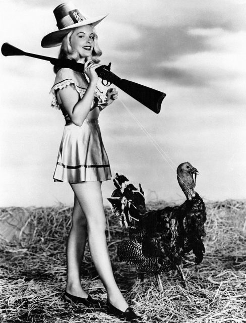 Barbara Bates holding a shotgun while walking a turkey on a leash