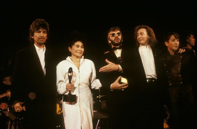 George Harrison, Yoko Ono and John Lennon standing on stage at the Rock and Roll Hall of Fame