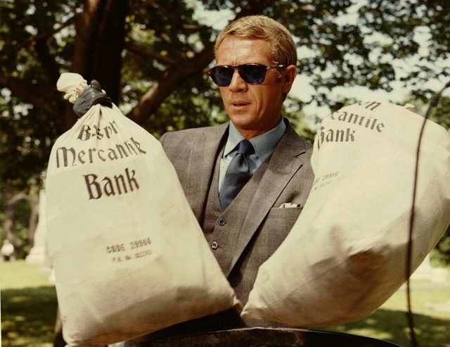 Thomas Crown holding up two bags of money