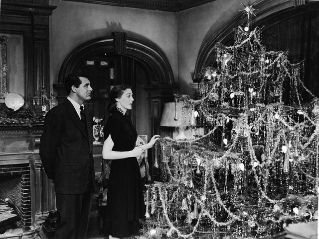 Cary Grant looks on as Loretta Young decorates a Christmas tree 