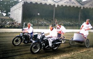 Men racing motorcycle chariots in front of spectators