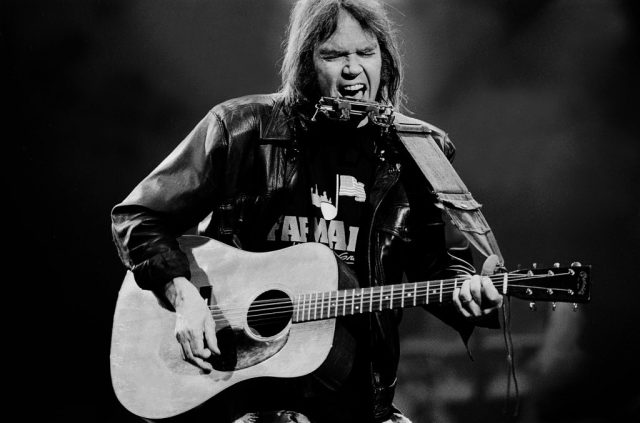 Neil Young performing with a guitar on stage