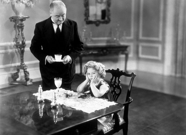 Barbara Barry frowning while sitting at a table with her butler
