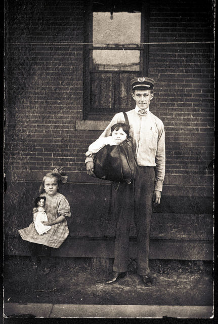Little girl sitting next to a postman with a young boy in his mailbag