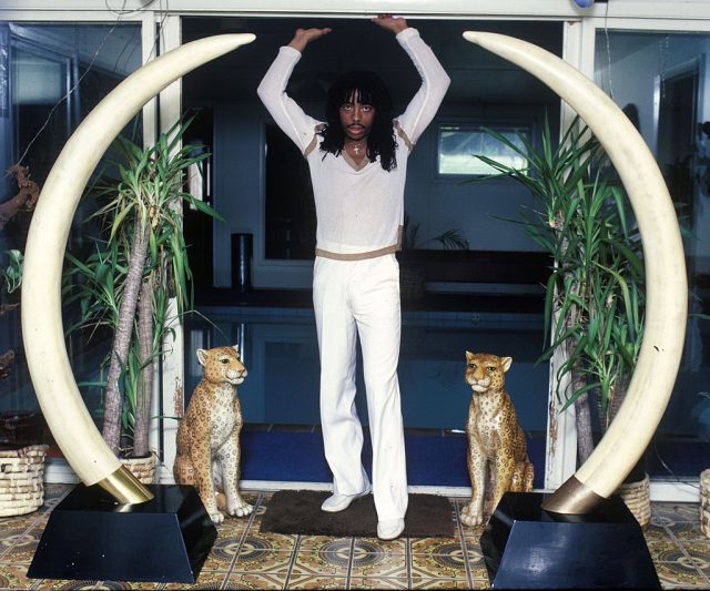 Rick James standing between two elephant tusks and two wildcat statues