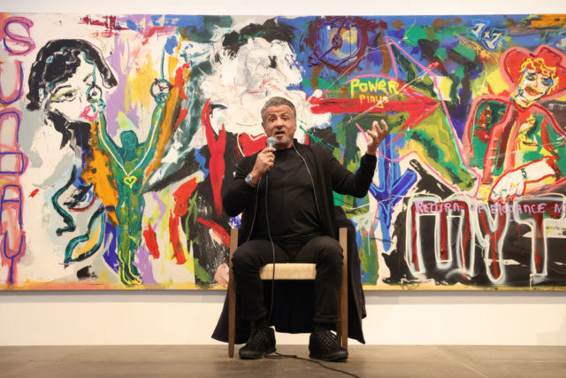 Sylvester Stallone speaking in front of his own painting