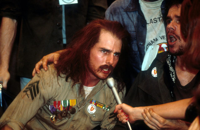 Ron Kovic leaning into a reporter's microphone