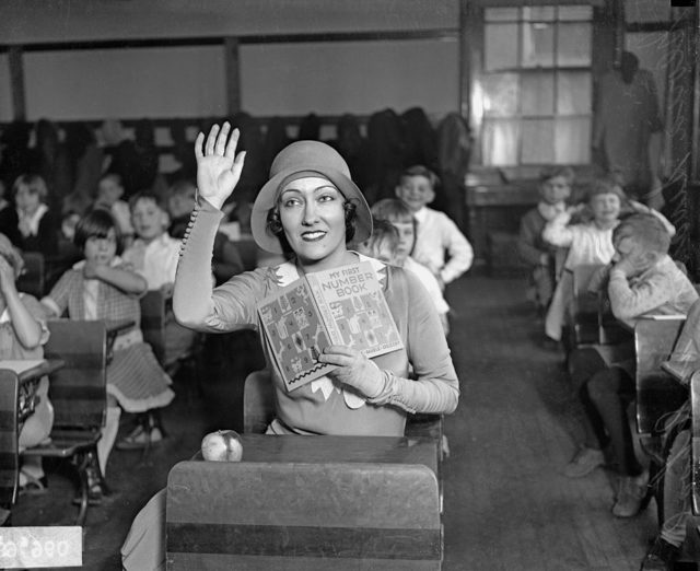 Gloria Swanson sitting at a desk in a classroom