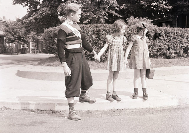A boy helping two little girls cross the street