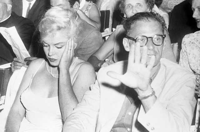 Movie queen Marilyn Monroe wears a bored expression as her playwright-husband Arthur Miller shoos photographers away at the Boston Arts Center Theatre on the banks of the Charles River here. They motored from their home at Roxbury, Conn., to see a performance of Macbeth. (Photo Credit: Bettmann / Contributor)
