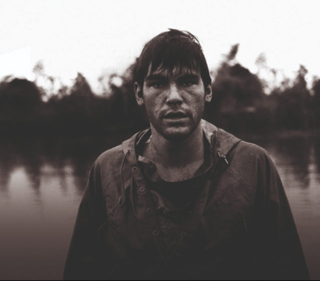 Oliver Stone standing in front of a body of water