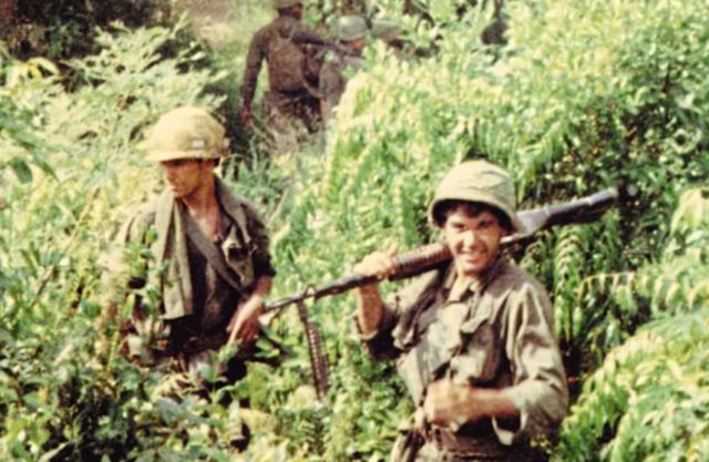 Oliver Stone standing in tall grass with his fellow servicemen