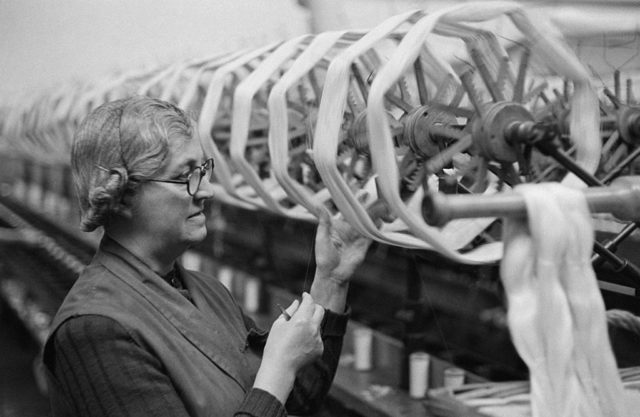 Elderly woman standing in front of a weaving machine