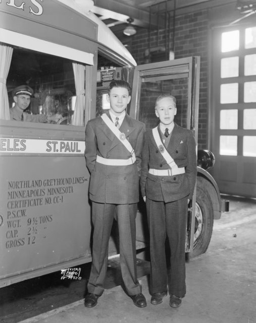 Two males School Safety Patrol members standing at attention beside a bus