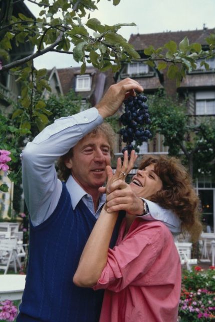 Gene and Gilda holding a bunch of grapes and laughing